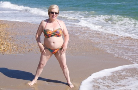 Mature UK woman Speedy Bee wears sunglasses while getting naked at the beach